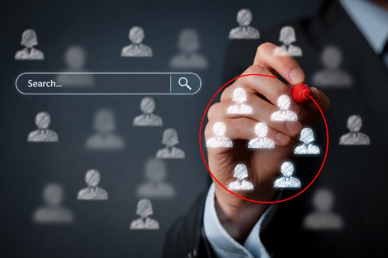A businessperson drawing a red circle around a cluster of highlighted people icons beside a search bar, illustrating pairing keywords with a target audience