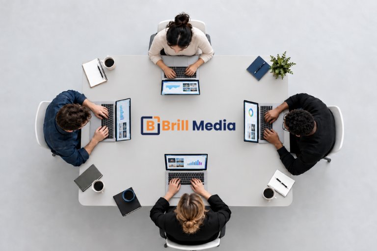 An overhead view of four team members working on laptops around a table centered with the Brill Media logo