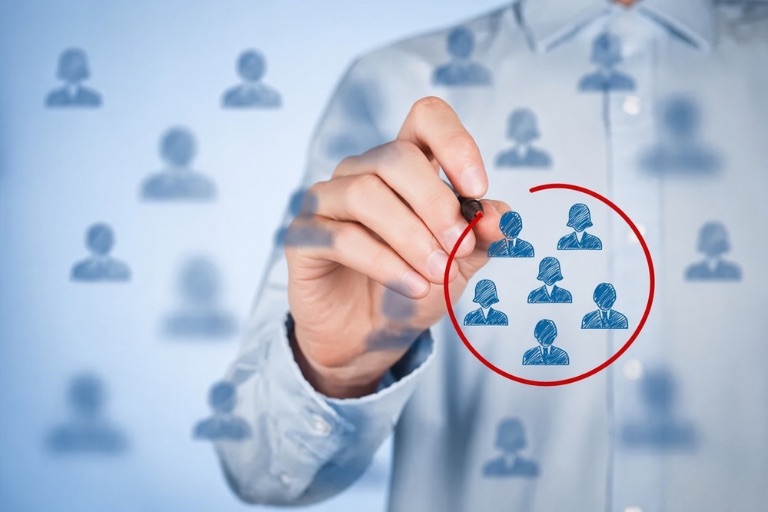 A hand drawing a red circle around one group of people among a crowd, illustrating selecting a specific audience segment