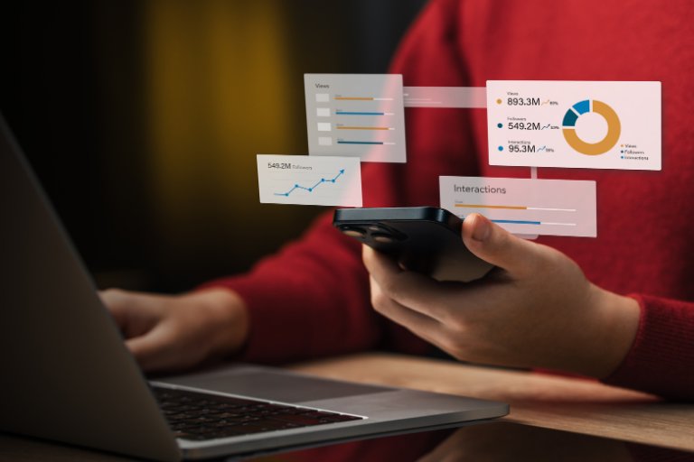A marketer at a laptop holding a phone, with floating cards showing views, followers and interactions metrics beside a donut chart